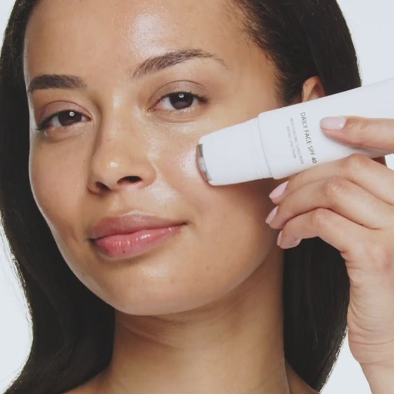 Vrouw brengt Daily Face SPF 40 aan met de metalen rollerball voor een gehydrateerde, stralende teint.