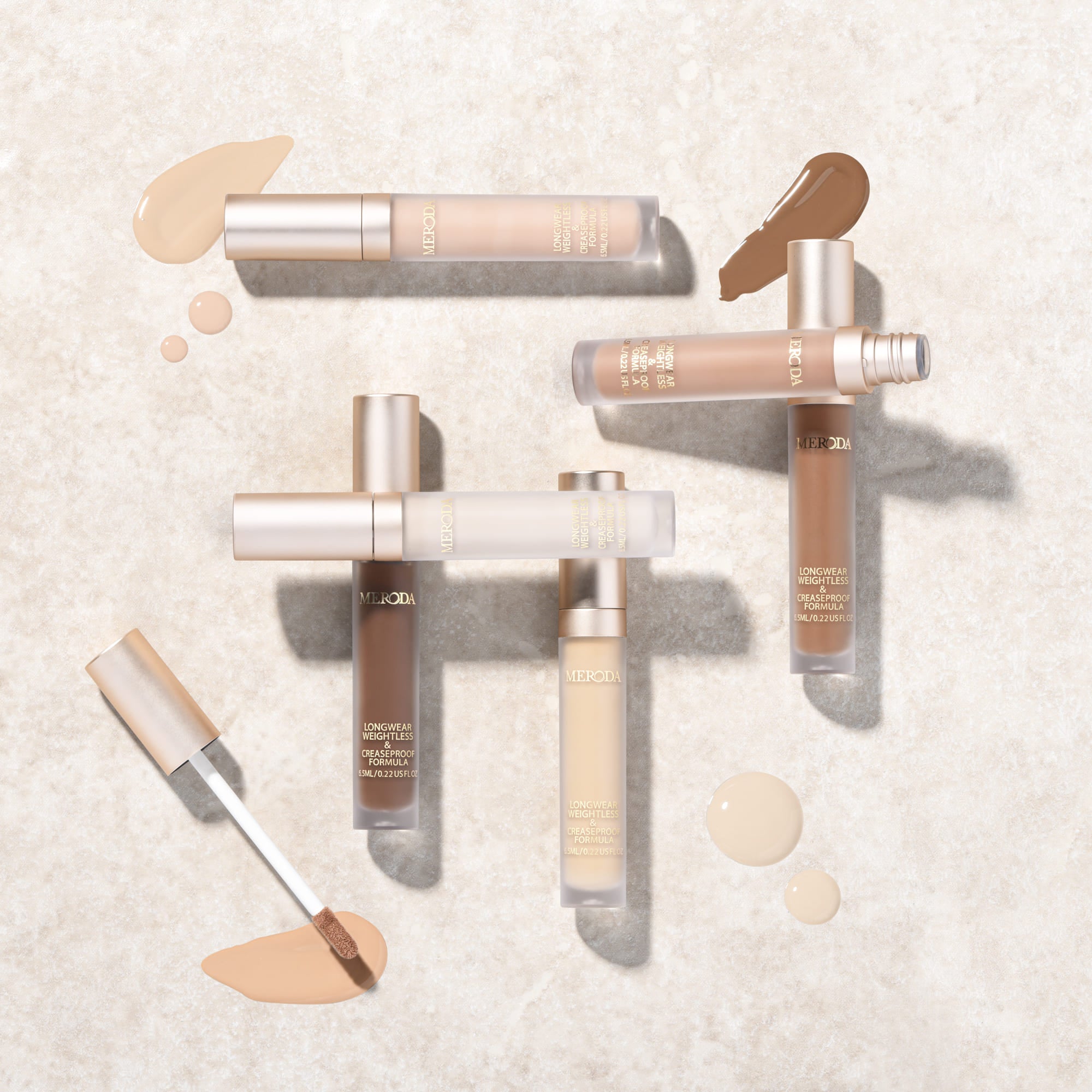 Universal Concealer tubes in verschillende tinten met vloeibare swatches en applicator op een lichte stenen achtergrond.