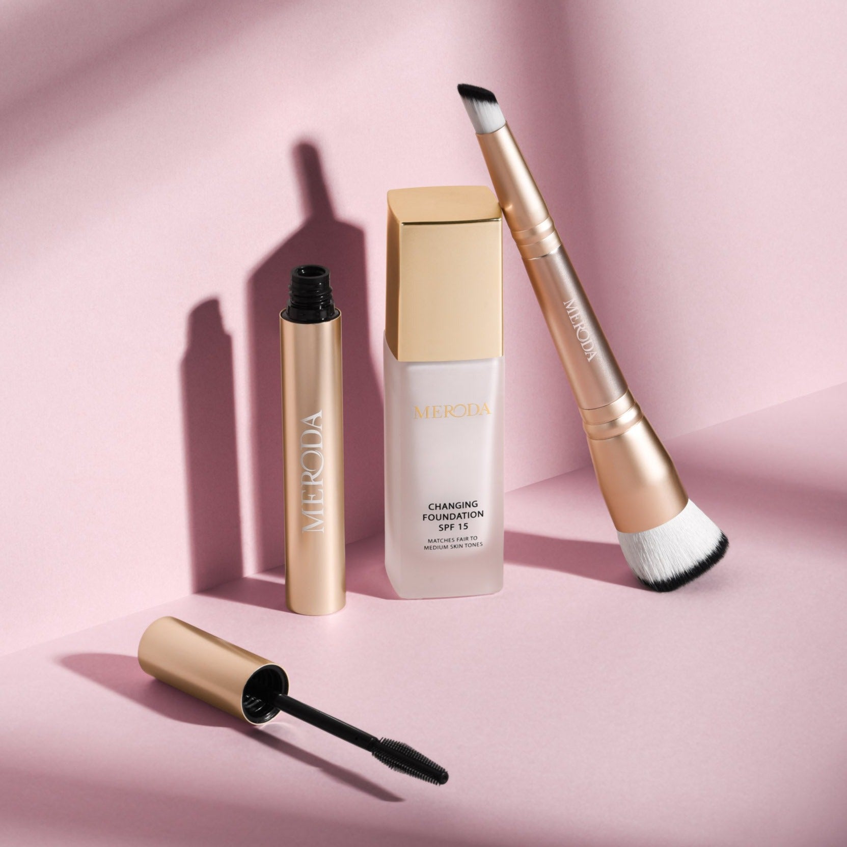 The Effortless Edit met Changing Foundation, Gilded Lashes Mascara en 2-in-1 Build & Conceal Brush op een roze achtergrond