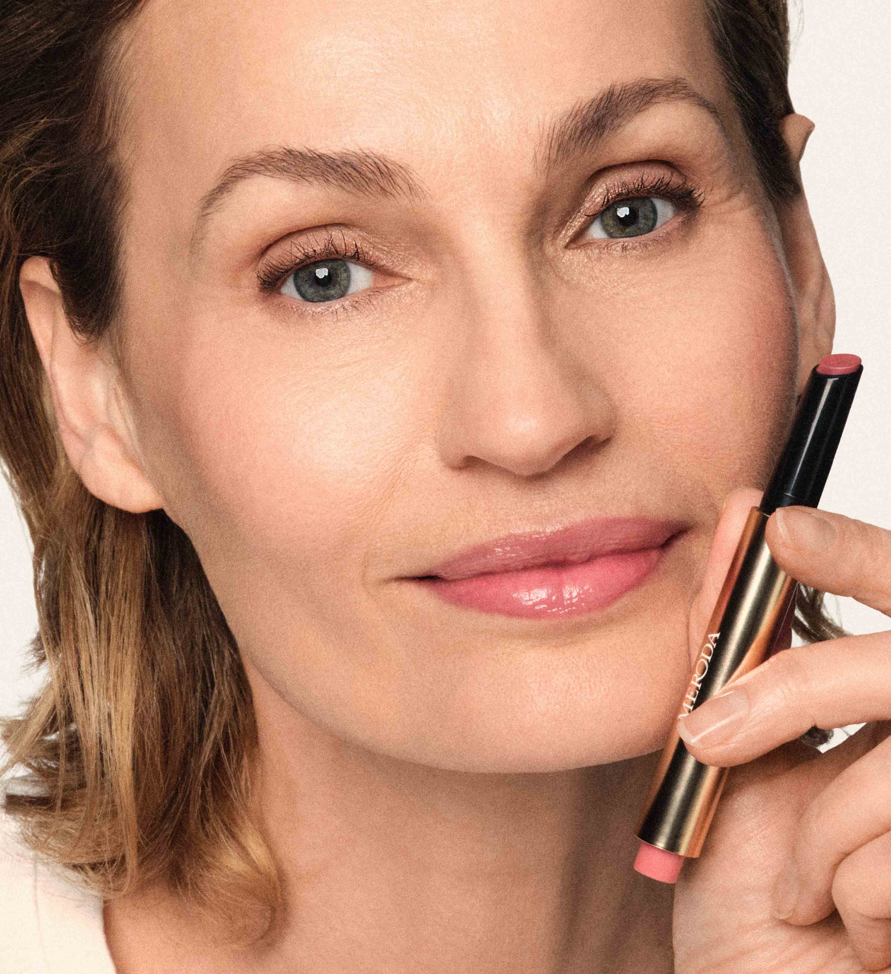 Model houdt de Hydrating Lip Tint in Dusty Rose bij haar gezicht voor glanzende lippen en een natuurlijke make-uplook.
