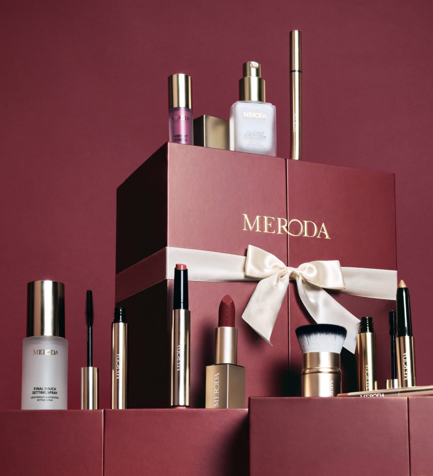 Bordeauxrode adventskalenderdoos met witte strik, omringd door diverse Meroda Cosmetics beautyproducten