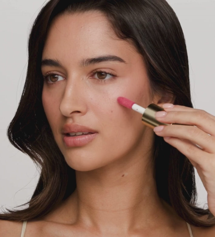 Model brengt en blendt de roze Vibrant Cheeks Liquid Blush uit The Valentines Bundle met een kwast voor een stralende gloed